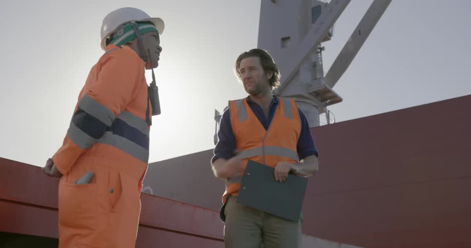 Two men wearing orange stand on a ship on a sunny day
