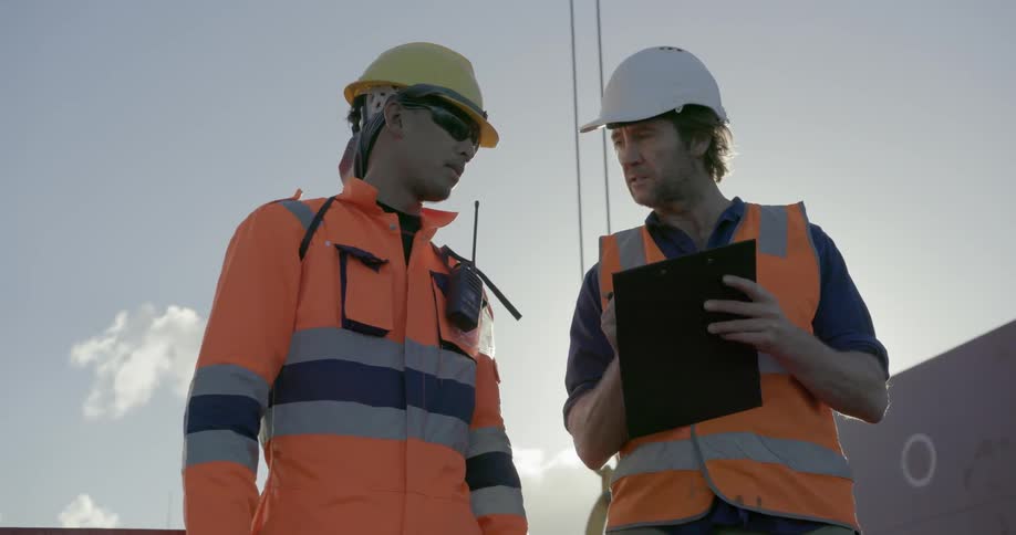 Two construction workers talk near a crane