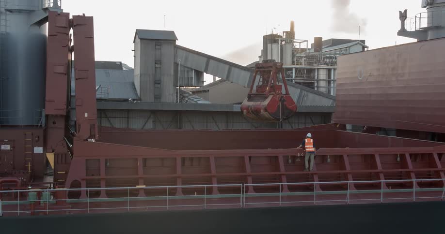 A man watches as a loader lifts materials from the hull of a ship