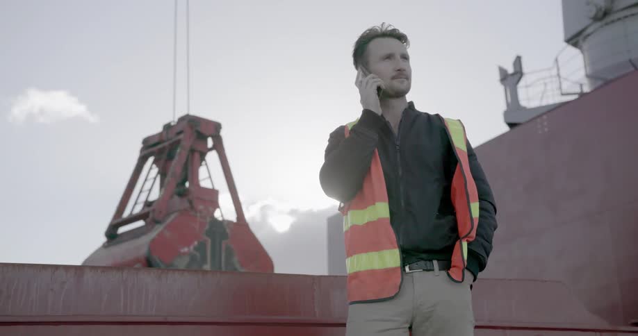 A worker talks on the phone while a crane lifts equipment behind him