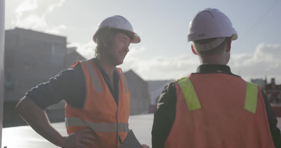 Two men stand on the deck of a ship having a discussion during the day