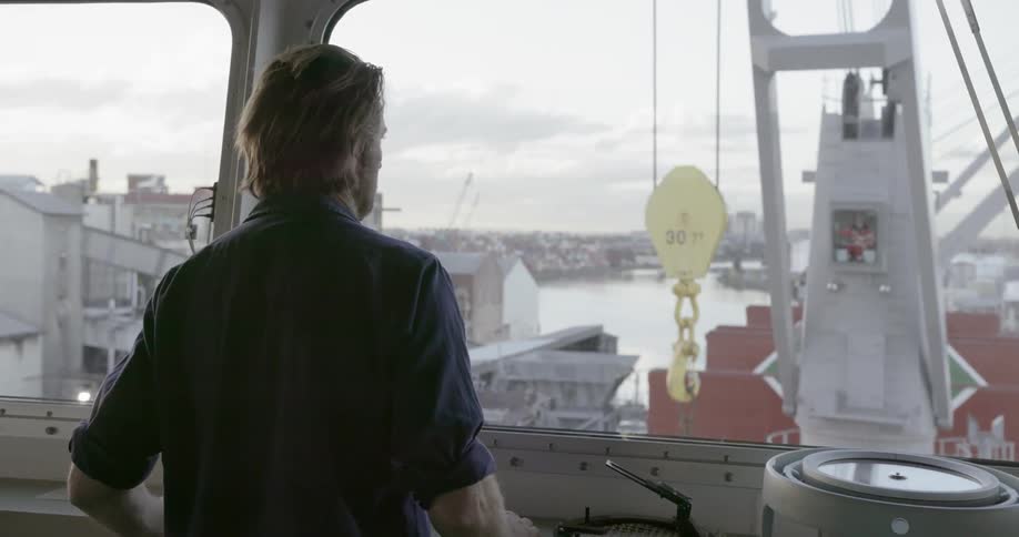 A man watches a crane from the bridge of a ship