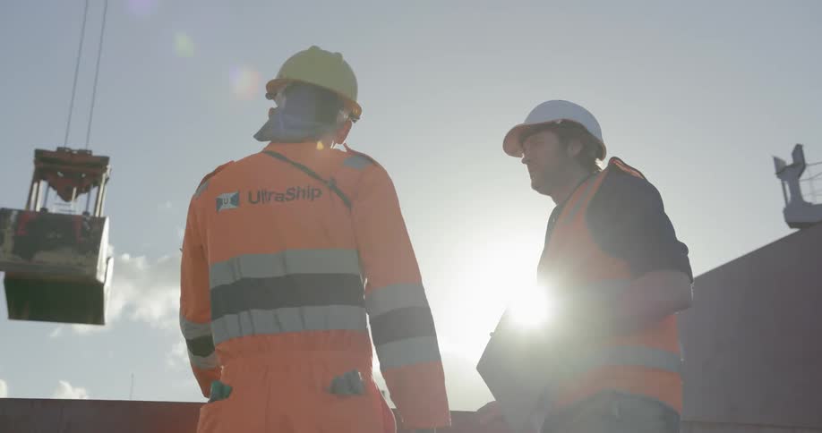 Two construction workers talk near a crane