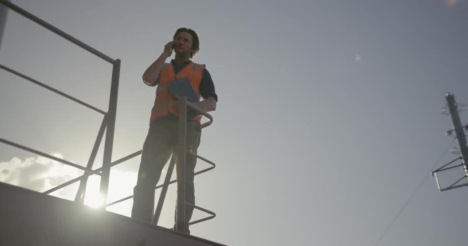 Man leans on a railing talking on his phone on a sunny day
