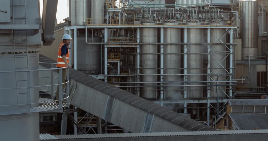 A construction worker leans against a rail at a factory