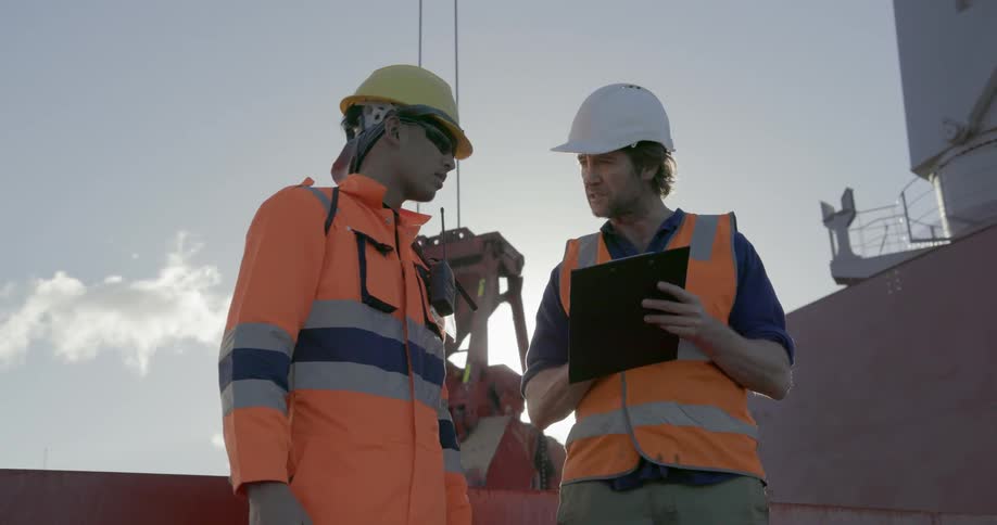 A man with a clipboard asks a construction worker questions and makes notes