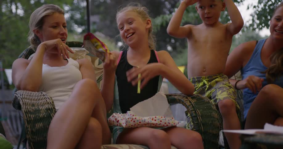 A group of kids are sitting outside and one is opening a present filled with candy
