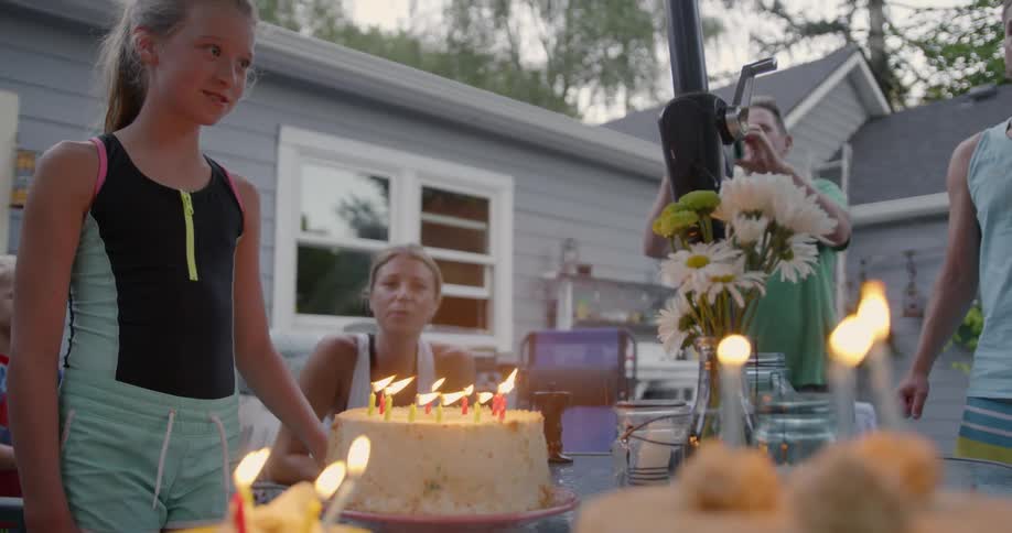 A young girl smiles as she blows out candles on a birthday cake