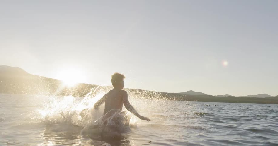 Two boys leap off a pier into a lake on a sunny day