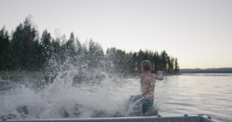 Boys run on a dock and jump into a lake at sunset