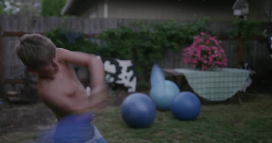 Boy throws a water balloon into the air and smashes it with a baseball bat