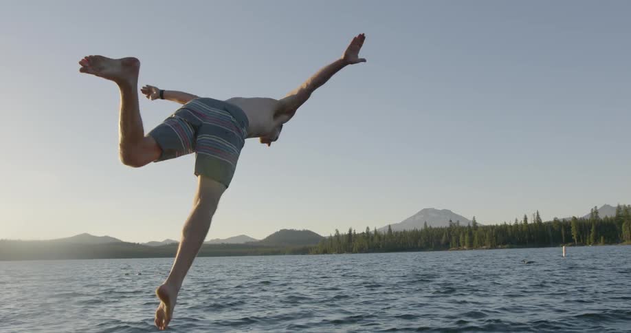 A teenager is jumping off a dock and into a lake