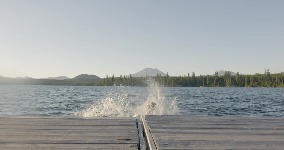 Two boys run on a dock and jump into a lake
