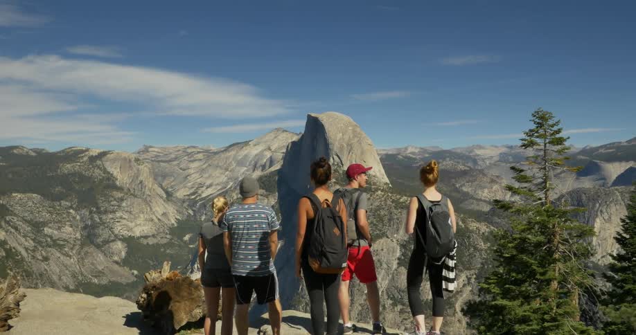 Group of people standing on a cliff overseeing a mountain range ahead