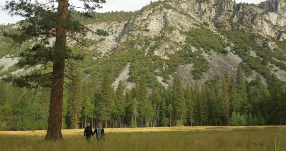 Two people holding hands walk away from a mountain