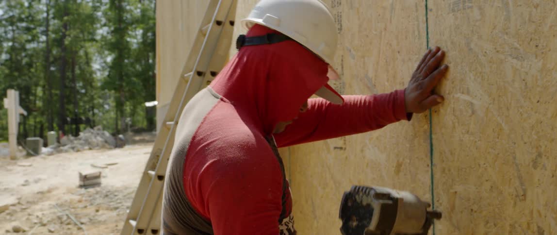 A man is using a nail gun to nail down a piece of lumber