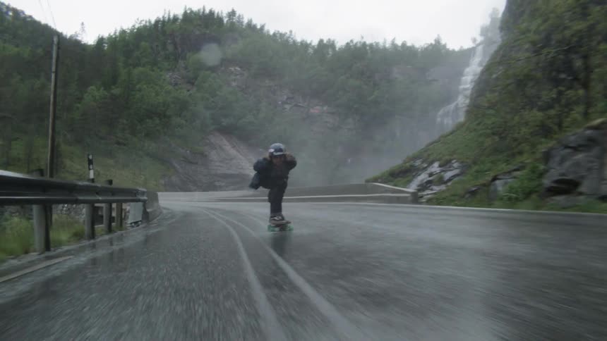 Person rides a skateboard down a long winding road
