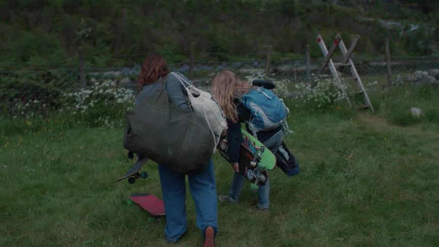 Two women are carrying supplies to a campsite next to a running stream