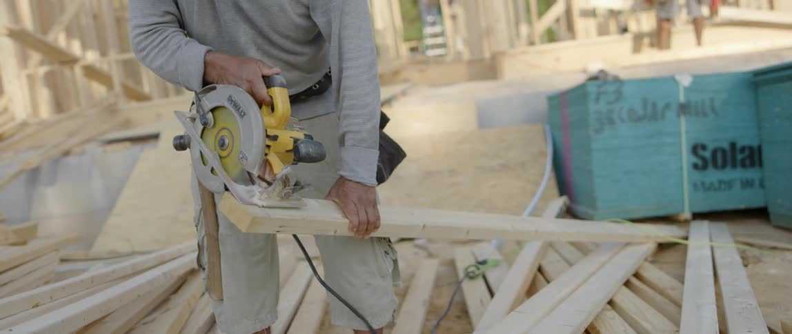 A construction worker cuts wood with a saw