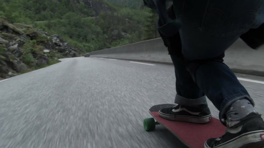 A skateboarder rides down a sloping road next to a guard rail