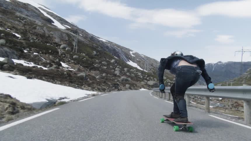 A skateboarder speeds down a mountain road