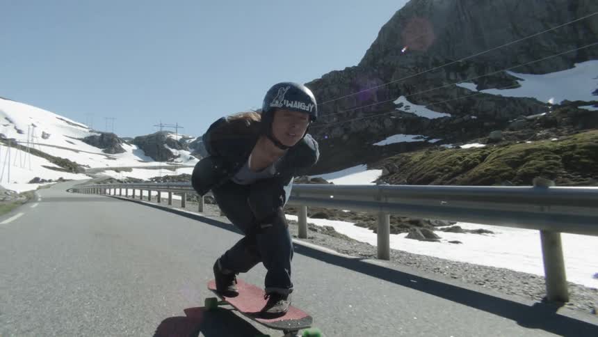 A woman is speeding down a mountain road on a skateboard in winter