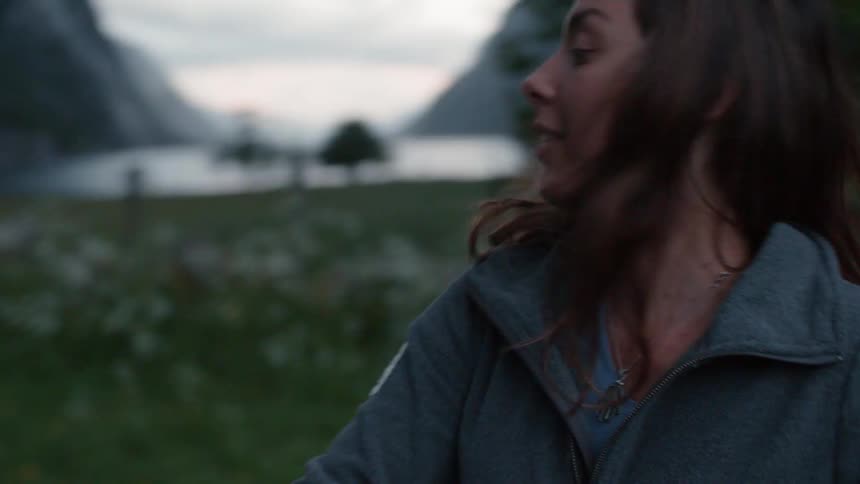 Two women are putting up a tent in a natural setting at dusk