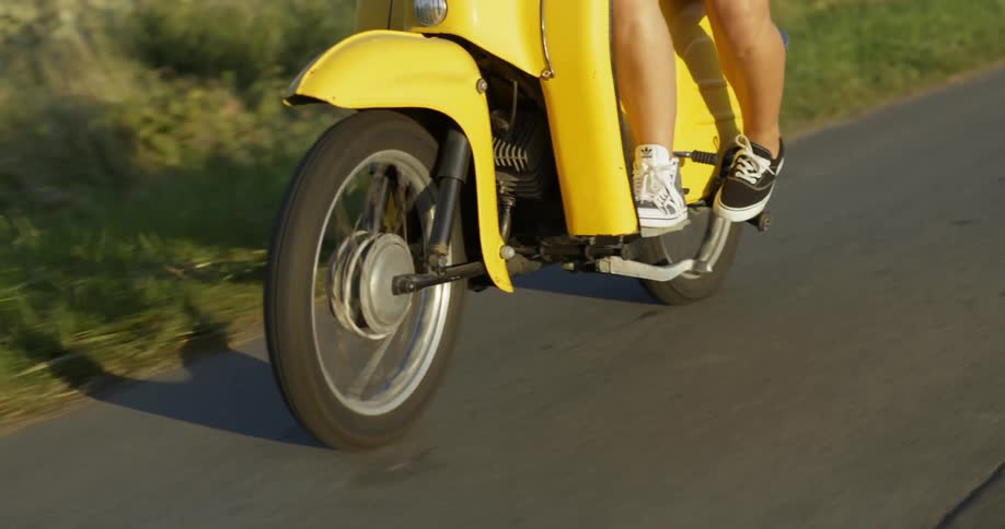 Two women are riding a moped on a country road during the day