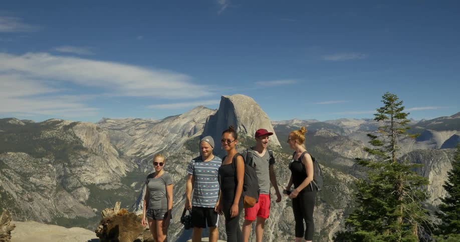 A group of people posing on a cliff with mountains behind them