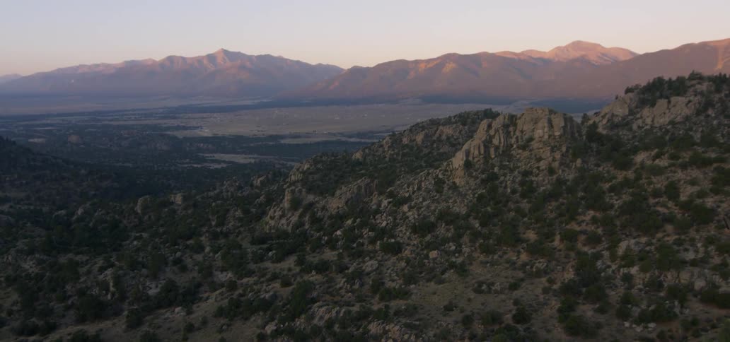 A rocky landscape with bushes and trees and a mountain on the horizon