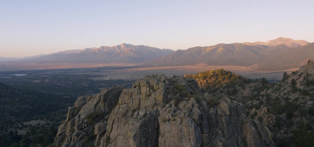 Rock pillar formations rise above a desert valley and mountain range at dusk