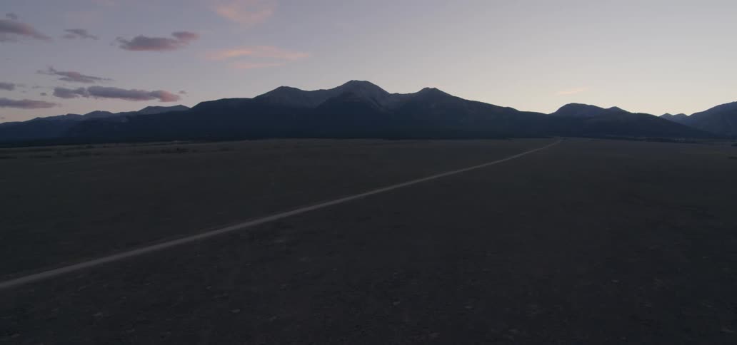 A long trail runs towards the mountains at sunset