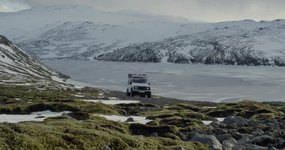 A white vehicle drives up a dark moody hill in Iceland