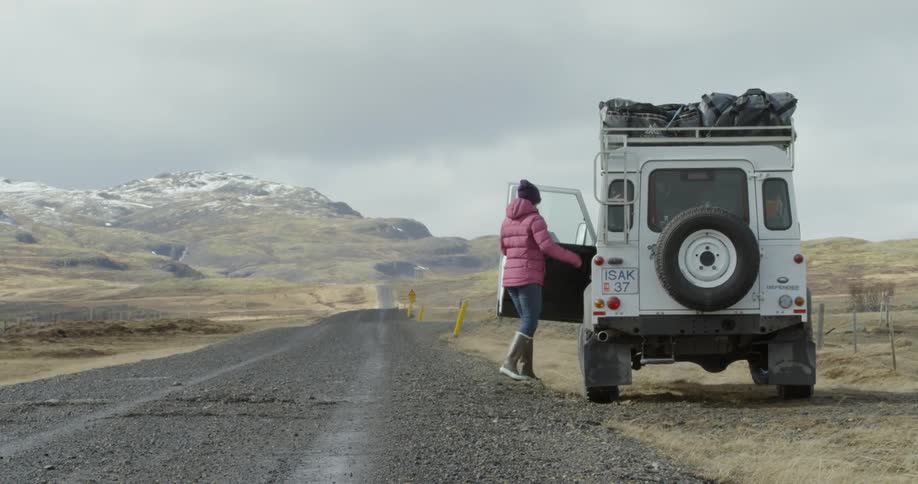 Woman opening a vehicle door and entering on the side of a dirt road