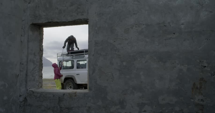 A man hands skis down to a person from a truck's roof rack