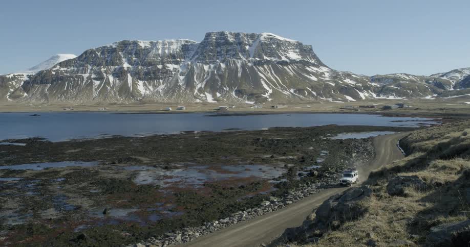 A vehicle drives on a dirt road in the rugged mountains by water