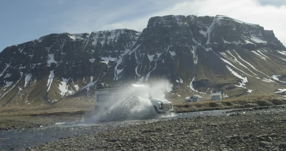 A white truck crosses a stream between mountains
