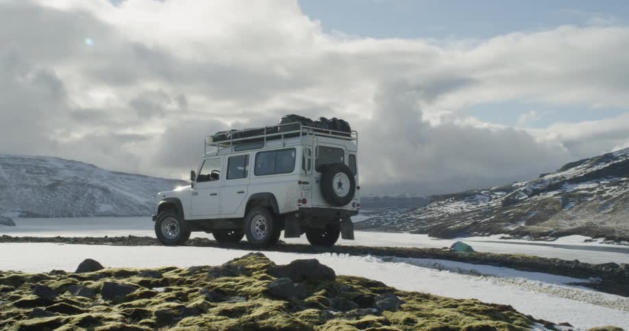 A woman drives a white jeep up a snowy hill in Iceland