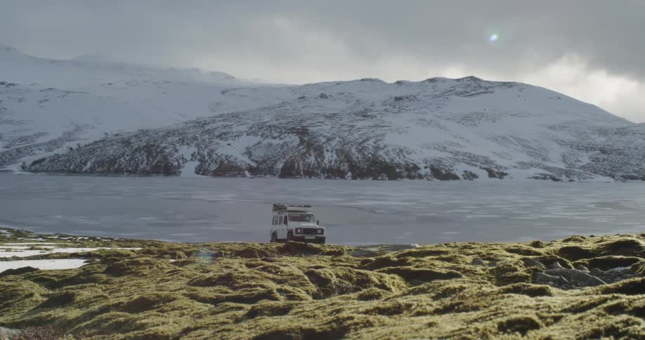 Jeep crosses green mossy landscape beneath snowy mountains