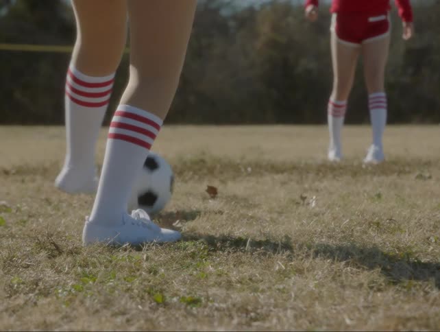 Two people kick a soccer ball out in a field