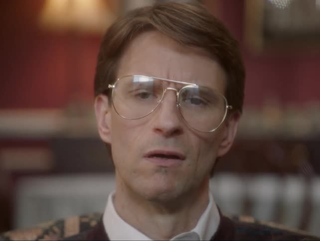 A man wearing glasses twists his head and blinks