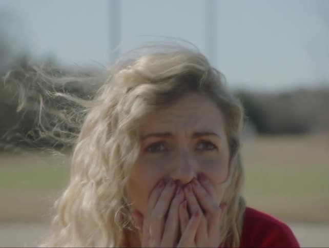 A teenage girl gasps and covers her face as she stands outside during the day