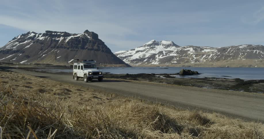 An suv travels down a dirt road near a lake