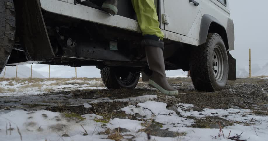 Person steps out of jeep onto snowy grass