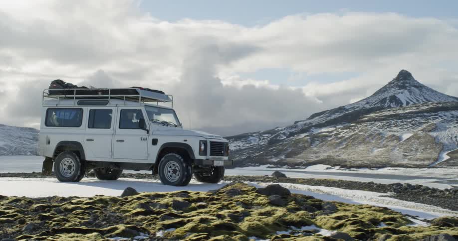 An suv with bags on roof travels down a snowy trail next to a frozen lake