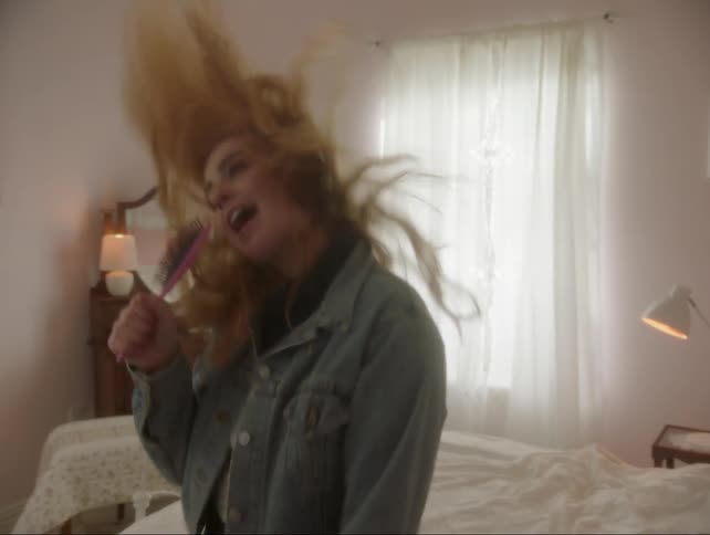 A teenage girl is dancing and singing in her bedroom