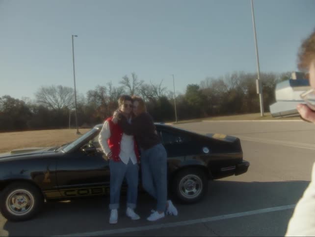 A man and woman pose for a photo by a sports car