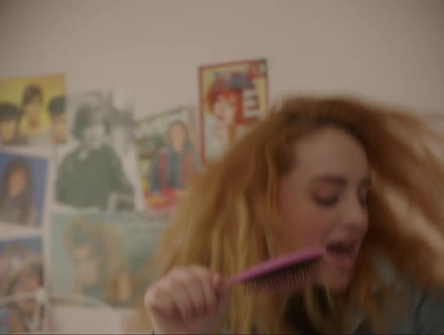 A teenage girl dances and sings into a hairbrush
