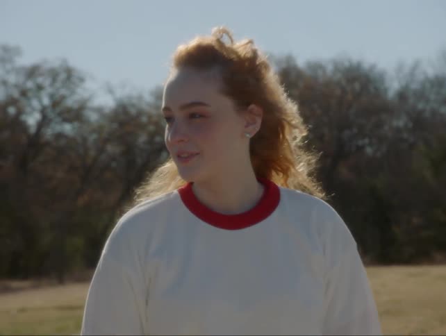 A teenage girl in a school uniform is smiling and looking to the side on a windy day