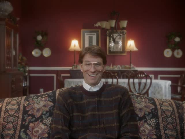 Man sits on a brocade couch laughing and shaking his head